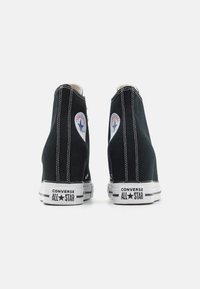 Svarta canvas hög-top sneakers med vitt broderi, klassisk logopatch på ankeln och svart-vitt gummisul med varumärkesbokstäver.