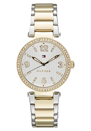 Złoty i srebrny zegarek na nadgarstek z pierścieniem wysadzanym kryształami, białą tarczą, złotymi znacznikami godzin oraz trzema wskazówkami pokazującymi godzinę 9:10:40, logo i nazwą marki na tarczy.