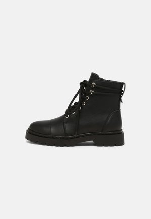 Bottine noire en cuir à lacets avec œillets en métal, semelle robuste et détails de couture, vue de côté sur fond blanc.
