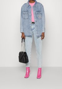 Camisa de mezclilla de color azul claro, camiseta rosa, jeans azul claro, botines rosas brillantes y un bolso acolchado negro con asas de cadena.