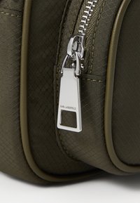 Borsa di tessuto verde texturizzato con zip e accessori in argento; presenta un'etichetta metallica con "KARL LAGERFELD" incisa. Design compatto e strutturato.