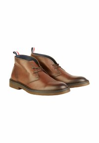 Bruine leren enkelboots met een gestructureerde afwerking, vetersluiting en een contrasterende marineblauwe voering. Rubberen zool met stiksel details.