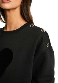 Sweatshirt noir avec un motif de cœur texturé à l'avant, doté de boutons dorés en accent sur les épaules et d'un col côtelé.