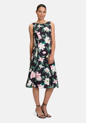 Blumenkleid mit schwarzem Hintergrund und pinken sowie weißen Blumen, ärmelloses Design, A-Linie Silhouette und knielanger Saum. Abgerundet mit schwarzen Absätzen.