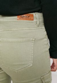 Olivgröna cargobyxor med en texturerad yta, med en sydd bakficka och en brun läderetikett "ONLY" på midjebandet.