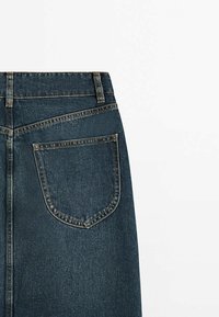 Vue arrière d'un jean en denim bleu foncé montrant une seule poche arrière avec des coutures visibles sur fond blanc.
