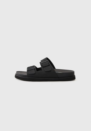 Schwarze Gummisandale mit zwei verstellbaren Riemen, einer strukturierten Fußbett und einer flachen Sohle. Minimalistisches Design mit klaren Linien.