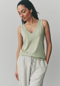 Top sin mangas de color verde claro con escote en V, hecho de tela suave, combinado con pantalones de chándal grises que tienen una cinturilla elástica y bolsillos laterales.