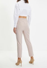 Geknipte witte blouse, lichtbeige getailleerde broek, gladde textuur, slim fit, met een rugventilatie detail. Gecombineerd met beige hoge hakken.