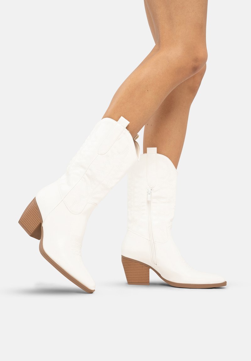 Botas de vaquero blancas con punta afilada, cierre de cremallera y un diseño texturizado. El tacón es marrón y de forma cuadrada, con ranuras verticales.