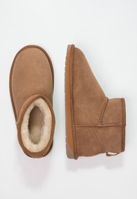 Stivali alla caviglia in suede marrone con una morbida fodera beige, punta arrotondata e suola in gomma testurizzata. Presentano un profilo basso e dettagli delle cuciture.