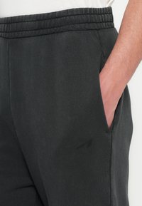 Tmavě šedé jogger kalhoty vyrobené z měkkého materiálu, s elastickým pasem, bočními kapsami a jemnými švy.