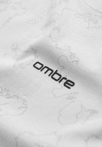 Gros plan sur un tissu blanc avec les contours pâles d'une carte du monde et le texte noir « ombre » imprimé dessus.