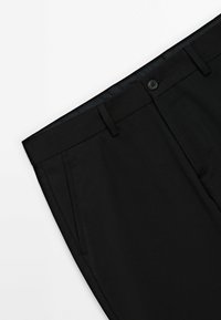 Pantalon noir sur mesure avec ceinture, passants de ceinture, poches latérales et fermeture par bouton sur fond blanc.