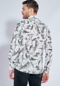 Langarmshirt in Creme mit schwarzem Blumen- und Pflanzenmuster, mit einem Kentkragen und Bündchen, strukturiertem Stoff.