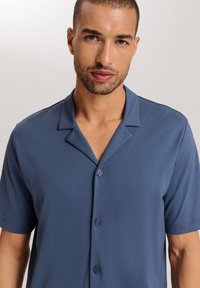 Modrá košile s krátkým rukávem vyrobená z hladké látky, s klopovým límcem a třemi předními knoflíky na zapínání. Jednoduchý design bez vzorů.