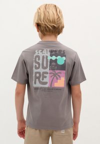 Graues Baumwoll-T-Shirt mit einem bunten Grafikdruck auf der Rückseite, der Palmen, einen Totenschädel und einen Text zeigt, der "SURF", "Scalpers" und "Entschuldigung, ich mache eine Pause" liest.