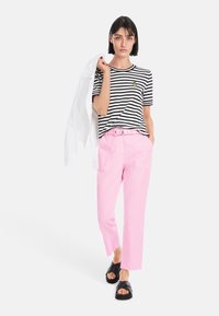 Striped black and white cotton T-shirt with a pineapple detail, paired with pink cropped pants and black slide sandals. White jacket draped over arm.