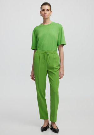 Camiseta verde de manga corta y corte relajado, combinada con pantalones verdes ajustados que presentan una cintura elástica. Zapatos negros de punta.