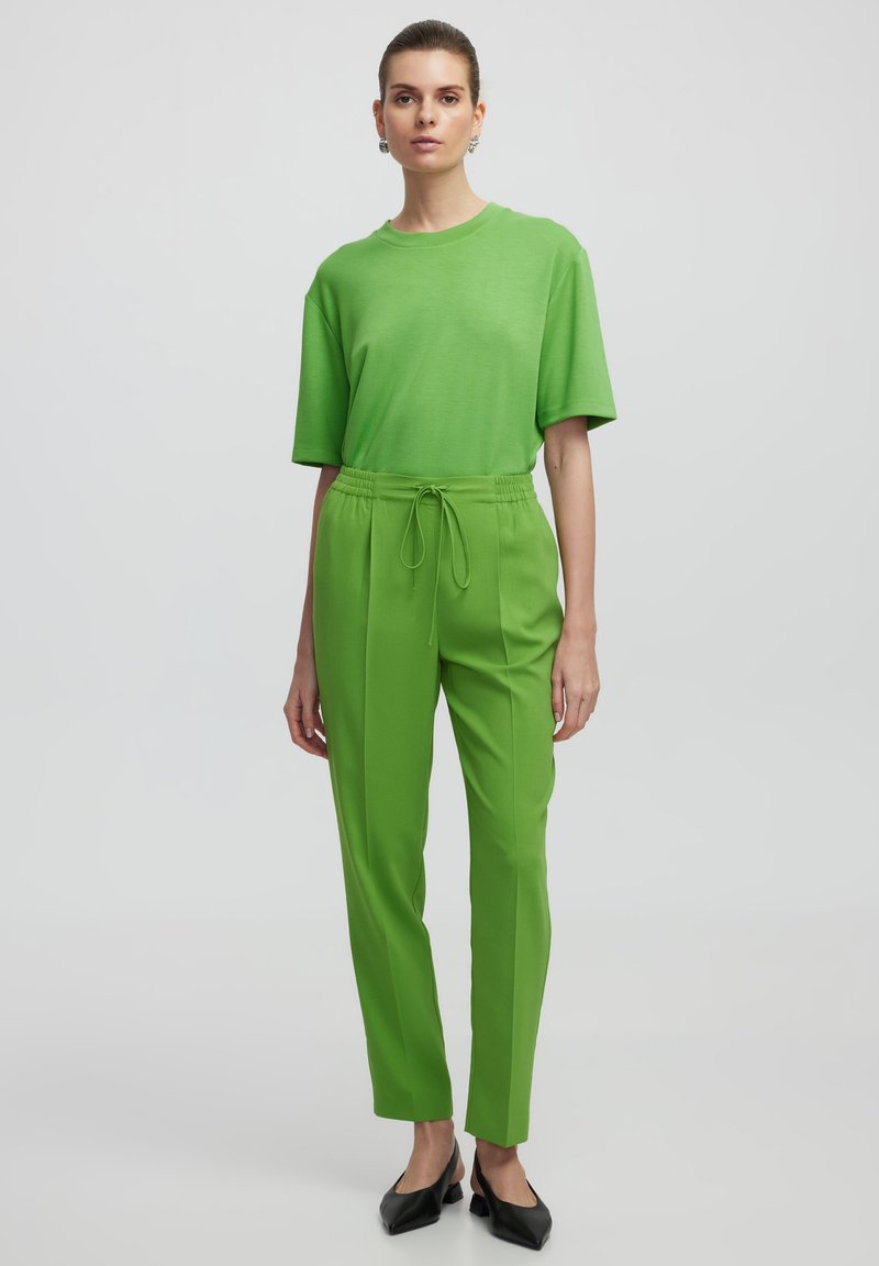 Groene T-shirt met korte mouwen en een ontspannen pasvorm, gecombineerd met bijpassende groene taps toelopende broek met een elastische tailleband. Zwarte puntige schoenen.