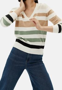 Pull à col en V avec des rayures horizontales beige, vert et blanc, et des accents noirs aux poignets et à l'ourlet. Fabriqué à partir d'un matériau doux.