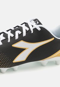 Melns futbola zābaks ar teksturētu virsmu, baltām šņorēm, izteiksmīgu balto un zelta logotipu un rakstainu papēdi ar vairākiem baltiem kājām.