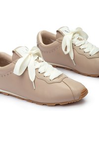 Baskets en cuir beige avec des lacets en coton blanc, bout rond, design minimaliste, petites accents en rivets et semelle en caoutchouc brun texturé.