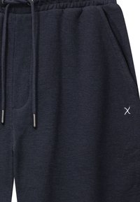 Tummansiniset collegehousut, joissa on elastinen vyötärönauha, kiristysnyörit, sivutaskut ja pieni valkoinen kirjailtu "X" reisiosassa.