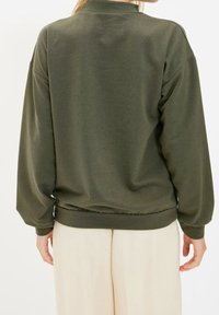 Olivgrön sweatshirt med hög krage, sänkt axel och ribbade muddarna. Materialet ser mjukt ut med en avslappnad passform.