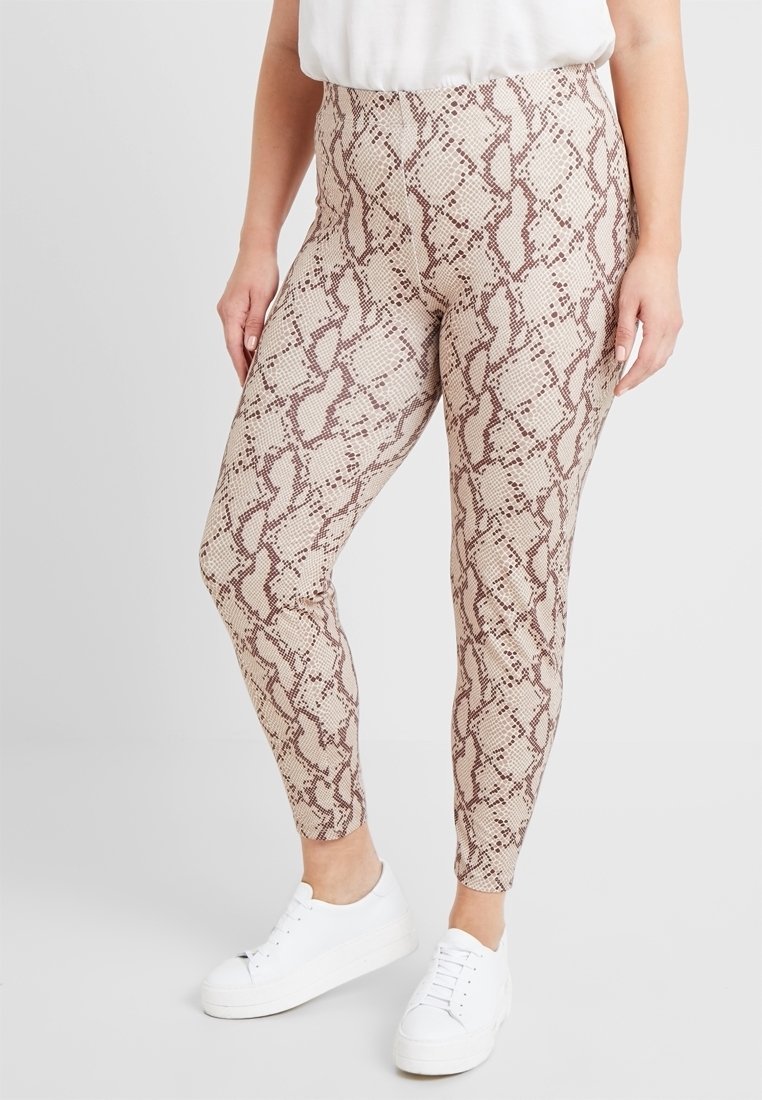 Leggings à motif peau de serpent en beige et marron, dotés d'une taille haute et d'une silhouette ajustée, associés à des baskets blanches.