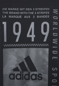 Musta kangast t-särk, millel on valge ja hall tekst ning graafika, sealhulgas "1949" ja Adidas logo kolme riba disainielementidega.