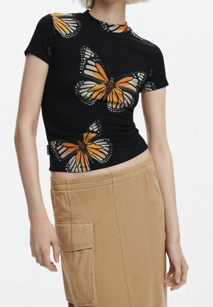 Top negro acanalado con estampado de mariposas en naranja y blanco, cuello redondo y mangas cortas. Combinado con pantalones estilo cargo en beige.