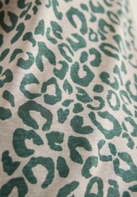 Motif léopard vert sur tissu beige clair, montrant la texture et de doux plis.