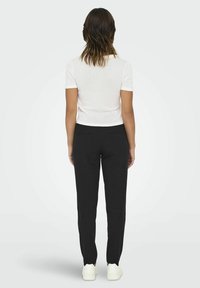 Top bianco a maniche corte abbinato a pantaloni neri e sneakers bianche. Il top è aderente, mentre i pantaloni hanno una silhouette sartoriale.