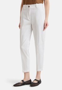 Donna che indossa pantaloni bianchi su misura alla caviglia con un top marrone e scarpe Mary Jane nere in rete con fibbie.