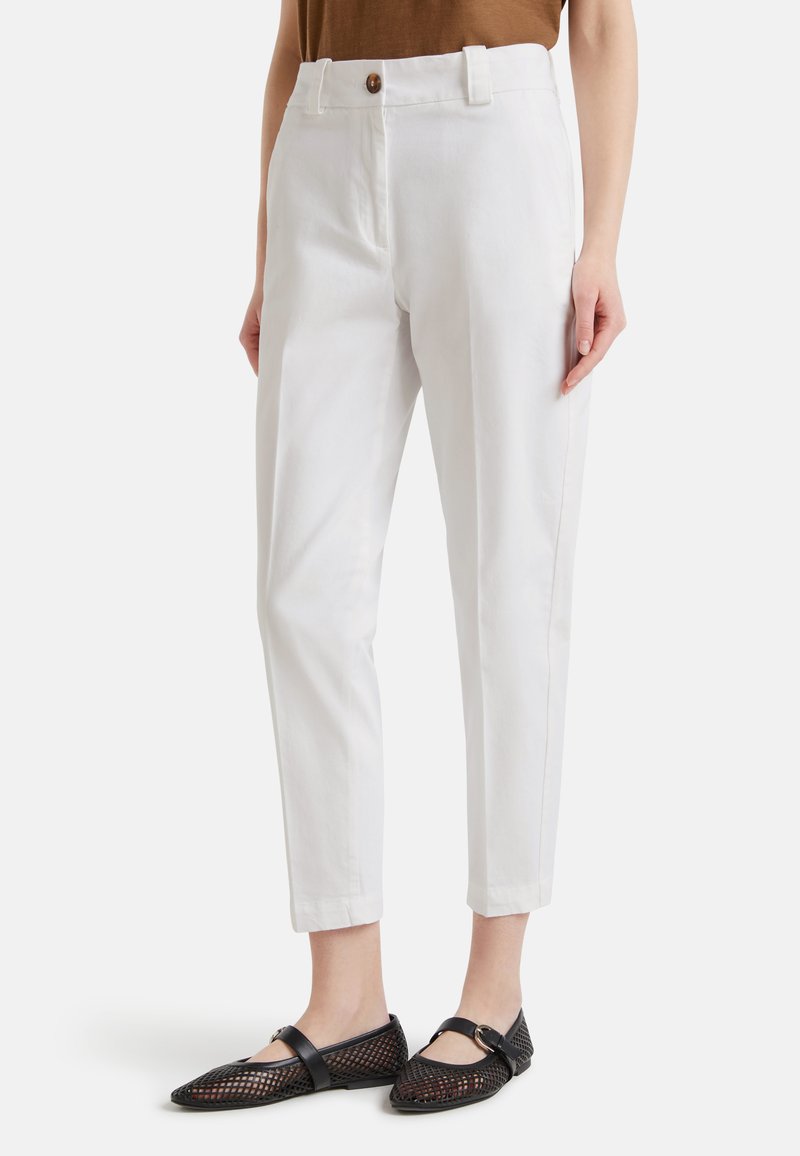 Donna che indossa pantaloni bianchi su misura alla caviglia con un top marrone e scarpe Mary Jane nere in rete con fibbie.