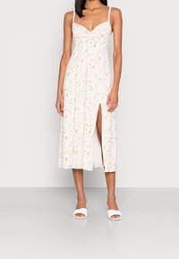 Vestido midi floral con un fondo rosa claro y acentos en verde y amarillo, un corpiño ajustado, tirantes finos y una abertura lateral.