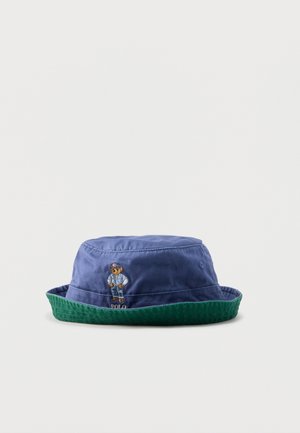 Pălărie tip bucket albastru și verde cu broderie cu urs purtând un costum albastru și textul „Polo” pe partea din față.