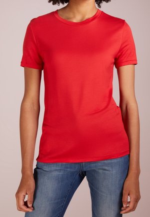 T-shirt rouge à manches courtes en tissu lisse avec un col rond. Coupe ajustée, design uni, porté avec un jean denim bleu.