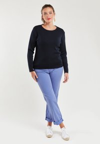 Maglione a maniche lunghe blu navy con scollatura a barca, abbinato a pantaloni azzurri risvoltati e sneakers bianche. L'outfit ha una texture morbida.