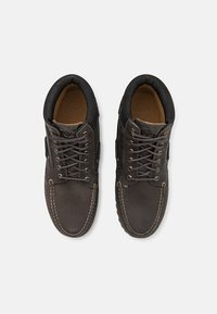 Donkere leren schoenen met een ronde vorm, voorzien van een vetersluiting, contrasterende stiksels en een gestructureerde zwarte kraag.