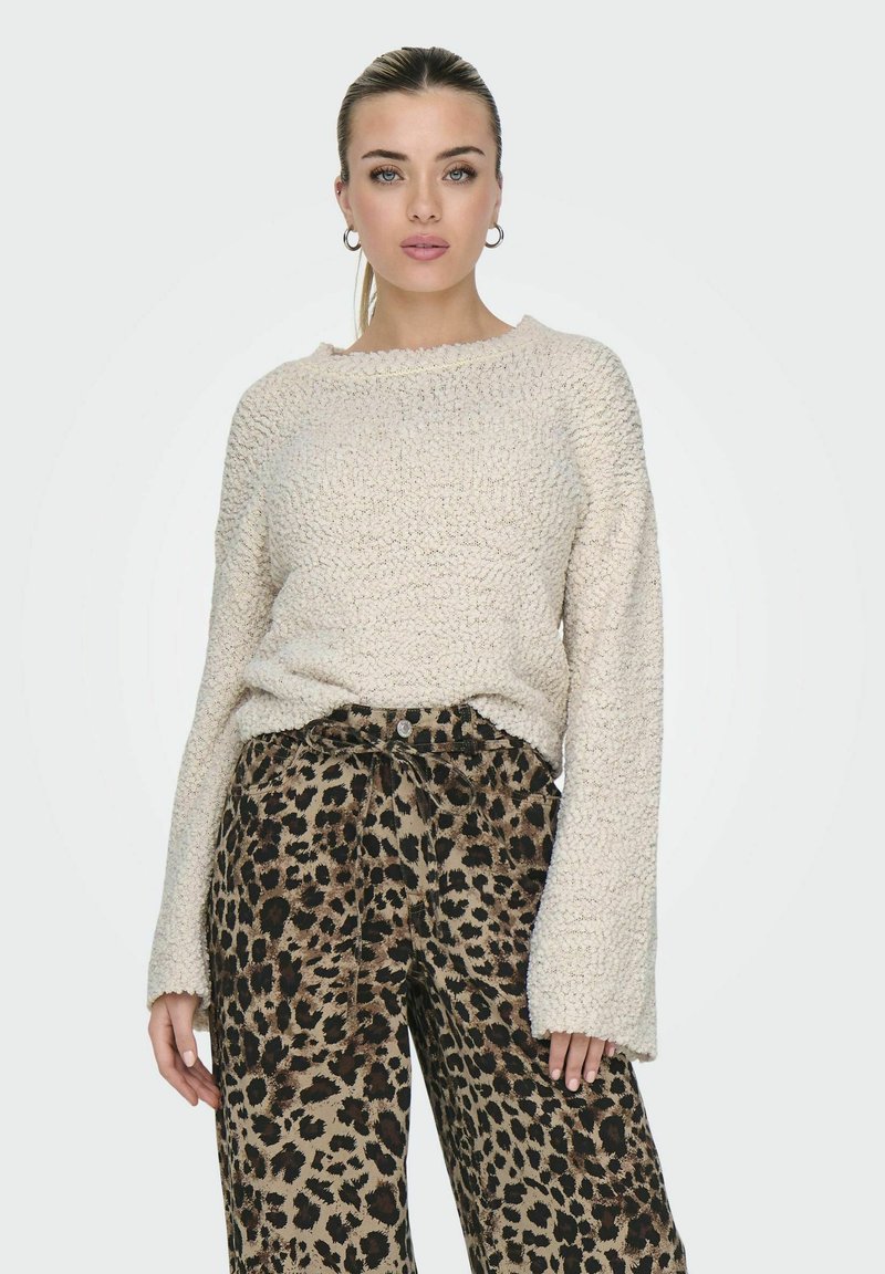 Maglione a maglia con texture crema e maniche ampie, abbinato a pantaloni a vita alta con stampa leopardata, dotati di una cintura annodata e chiusura con bottoni.
