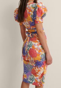 Robe à manches bouffantes à motifs floraux en orange, rose, violet et vert. Design ajusté avec une taille à nouer et des motifs floraux variés, longueur genoux. Tissu doux.