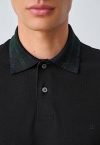 Juoda polo marškinėliai su tekstūruotu, languotu apykakliu žalių ir mėlynų atspalvių, su trimis juodais mygtukais ir subtiliu logotipo detaliu ant audinio.