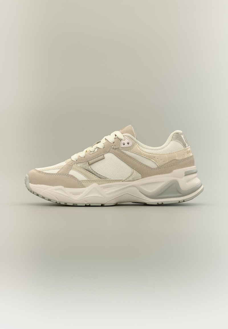 Baskets sportives beige et blanches avec des panneaux en mesh et en suède, des lacets blancs et une semelle épaisse et rembourrée sur un fond neutre.