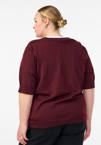Bordeauxroter Kurzarm-Pullover mit Rundhalsausschnitt und gerippten Bündchen. Weiche Textur, lockere Passform und minimale Nahtdetails.