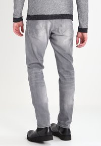 Pantalon en denim gris avec une coupe slim, doté de poches arrière, d'un léger délavage et d'une texture subtile, associé à des bottines noires.