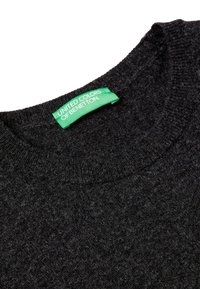 Czarny dżersejowy sweter z dekoltem, z zieloną metką marki United Colors of Benetton wszytą wewnątrz kołnierza.