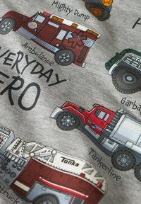 Ilustracije hitnih i komunalnih vozila s oznakama uključujući ambulantna kola, cisternu, kamion za odvoz smeća i vatrogasno vozilo na sivoj tkanini.