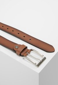 Ceinture en cuir marron avec boucle en métal argenté, dotée de plusieurs trous et d'une texture lisse. Comprend un accent métallique circulaire près de la boucle.